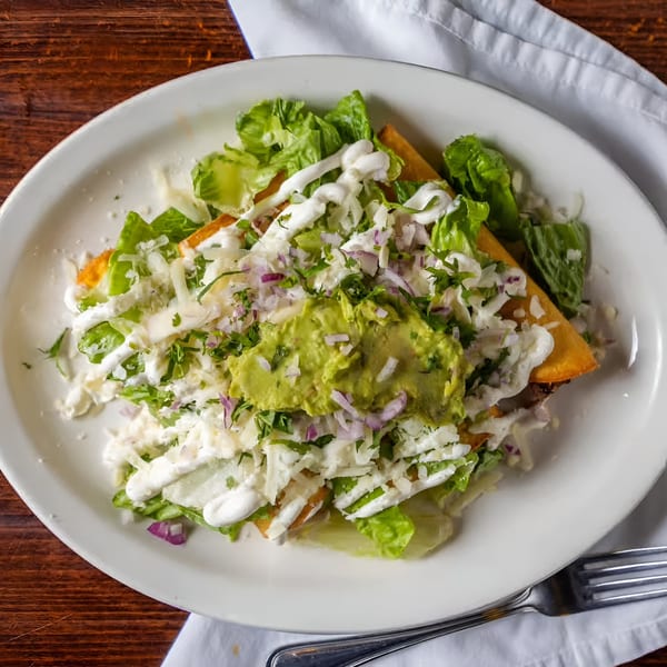 Los Mayas' Mexican tostada with lettuce, cheese, sour cream, guacamole, and red onion.