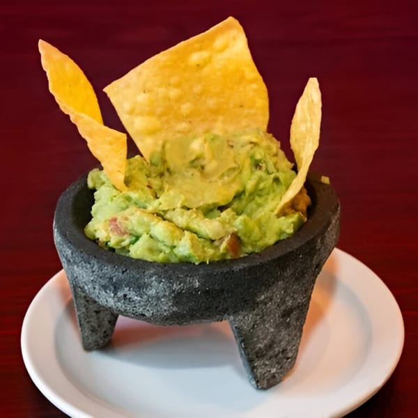 Los Mayas' guacamole in a molcajete with tortilla chips, on a white plate.