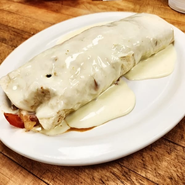 A Los Mayas burrito covered in white sauce and cheese, with red tomatoes visible on a white plate.