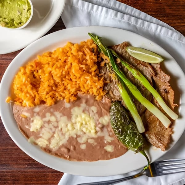 Los Mayas' carne asada with rice, refried beans, grilled onions, jalapeño, and a lime wedge.